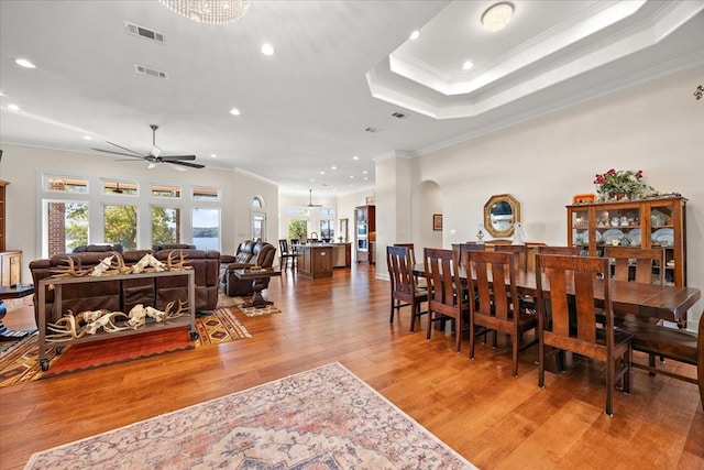 dining room featuring a raised ceiling, crown molding, hardwood / wood-style floors, and ceiling fan with notable chandelier