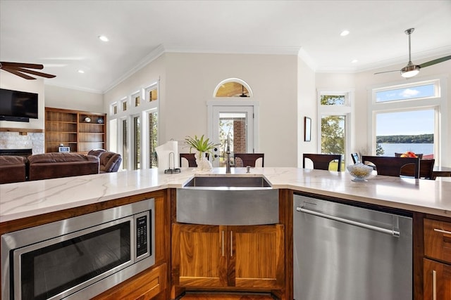 kitchen with a water view, sink, light stone countertops, ornamental molding, and appliances with stainless steel finishes