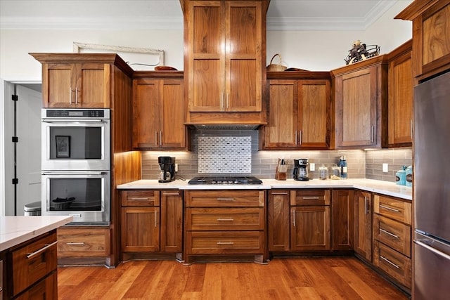 kitchen with backsplash, crown molding, stainless steel appliances, and hardwood / wood-style flooring