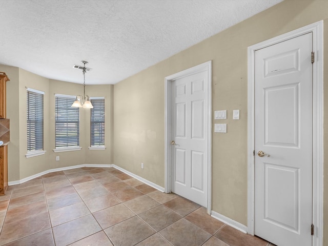 spare room featuring light tile patterned floors, a textured ceiling, and a notable chandelier