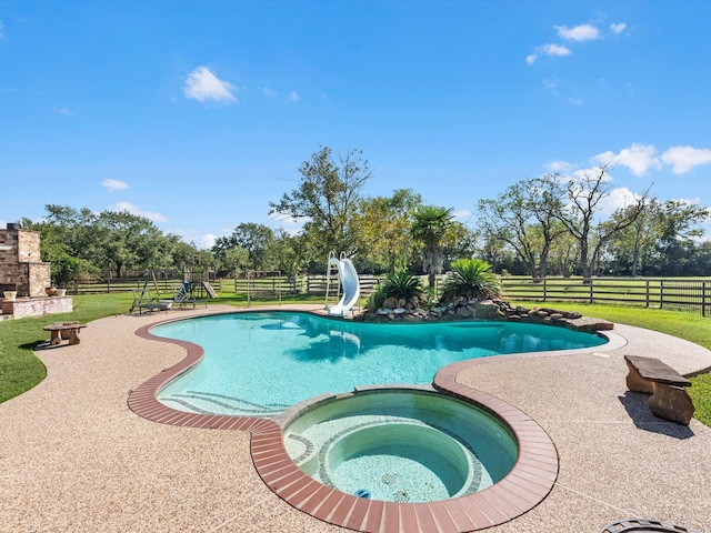 view of swimming pool with an in ground hot tub, an outdoor stone fireplace, a patio area, and a water slide