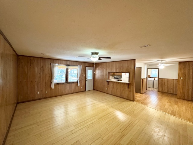 unfurnished living room featuring a textured ceiling, ceiling fan, wooden walls, washer and dryer, and light hardwood / wood-style flooring