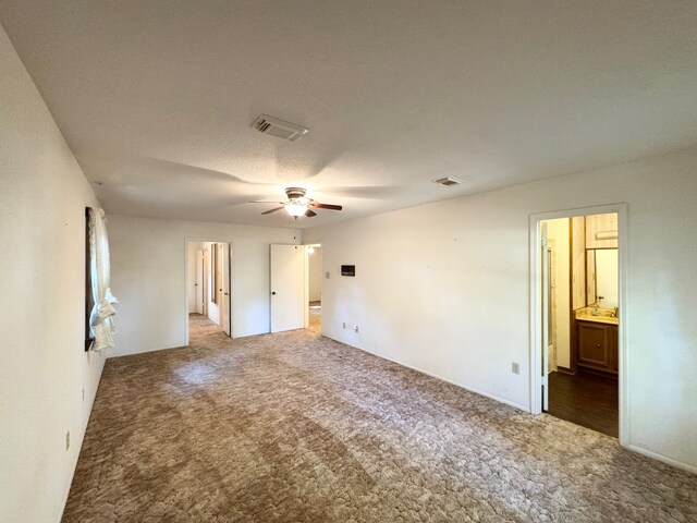unfurnished bedroom featuring dark carpet, a textured ceiling, ensuite bath, and ceiling fan