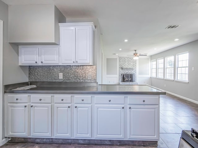 kitchen with decorative backsplash, a brick fireplace, ceiling fan, dark tile patterned flooring, and white cabinets