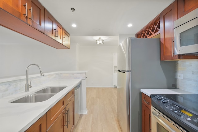 kitchen with light wood-type flooring, tasteful backsplash, light stone counters, stainless steel appliances, and sink