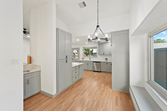 kitchen with stainless steel dishwasher, hanging light fixtures, a wealth of natural light, and light hardwood / wood-style flooring