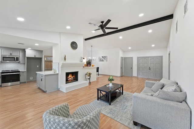 living room with a fireplace, ceiling fan with notable chandelier, vaulted ceiling, and light wood-type flooring