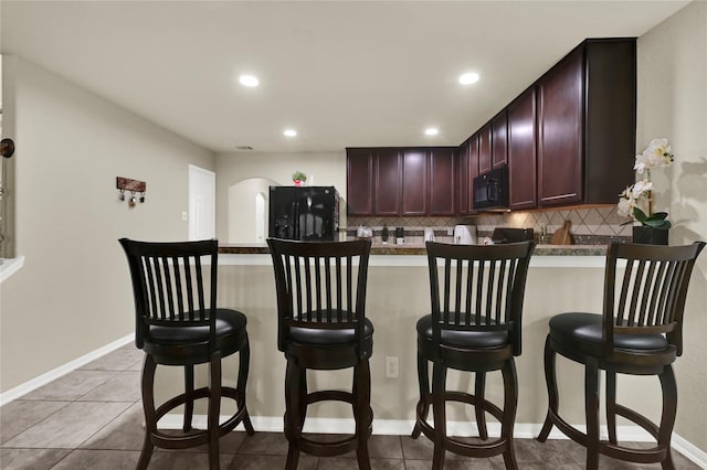 bar with decorative backsplash, light tile patterned floors, and black appliances