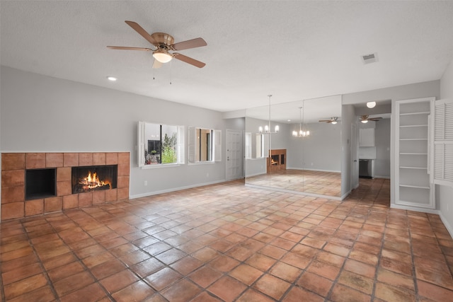 unfurnished living room with tile patterned floors, a tiled fireplace, a textured ceiling, and ceiling fan with notable chandelier