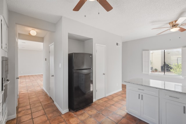 kitchen with white cabinetry, black fridge, ceiling fan, and light stone counters