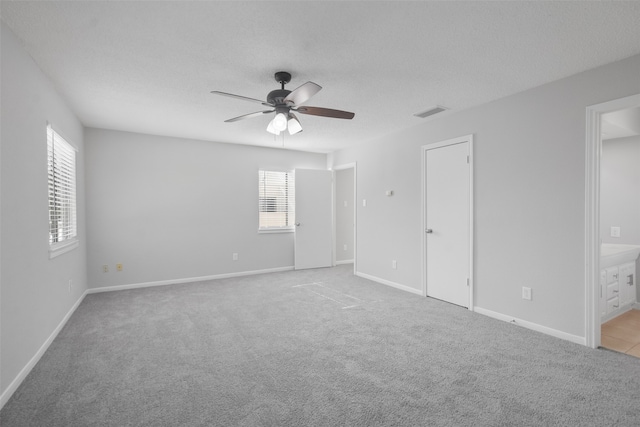 unfurnished bedroom featuring a textured ceiling, light colored carpet, ensuite bath, and ceiling fan