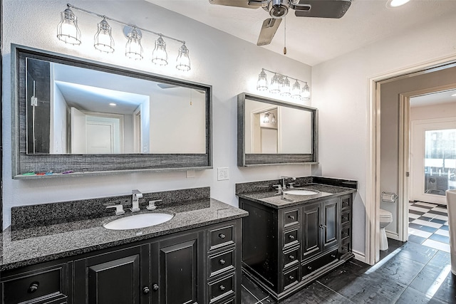 bathroom with a sink, toilet, two vanities, and a ceiling fan