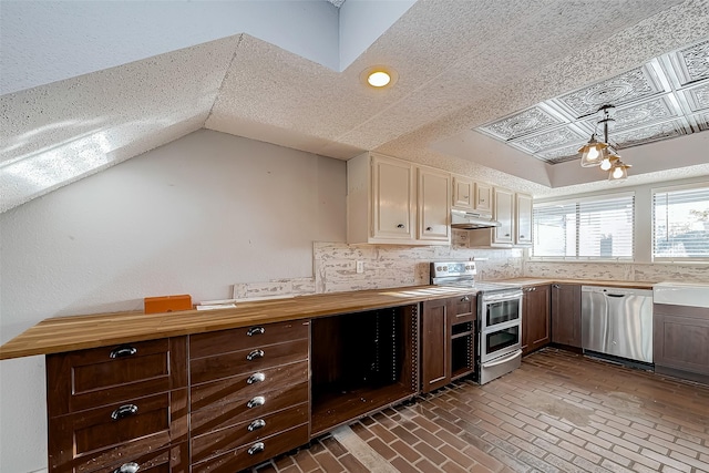 kitchen with tasteful backsplash, under cabinet range hood, butcher block countertops, brick floor, and stainless steel appliances