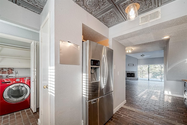 kitchen with a ceiling fan, visible vents, washer / clothes dryer, brick floor, and stainless steel fridge