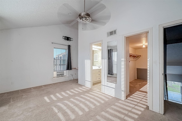 unfurnished bedroom with a spacious closet, visible vents, light colored carpet, lofted ceiling, and a textured ceiling