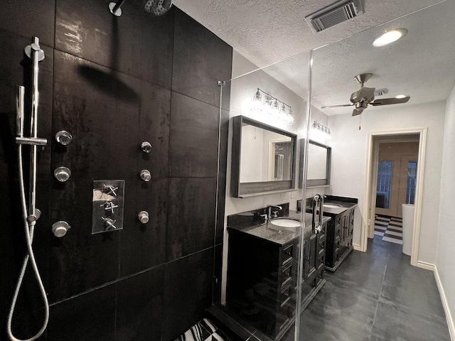 full bath with visible vents, double vanity, a tile shower, a textured ceiling, and a ceiling fan