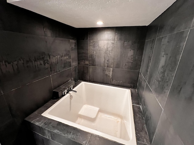 bathroom with tile walls, a bath, and a textured ceiling