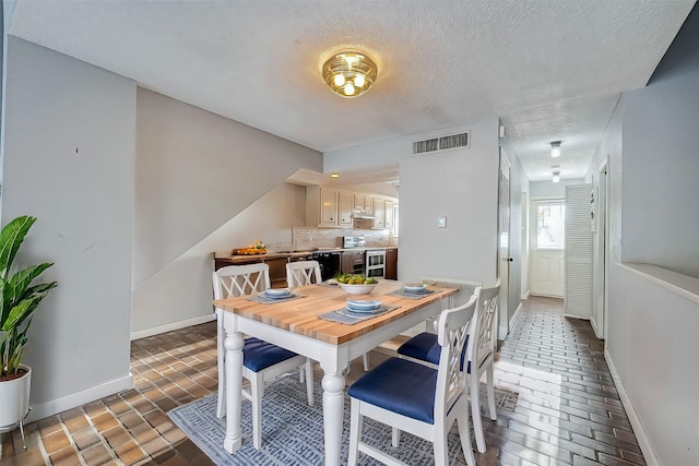 dining area with visible vents, a textured ceiling, brick floor, and baseboards