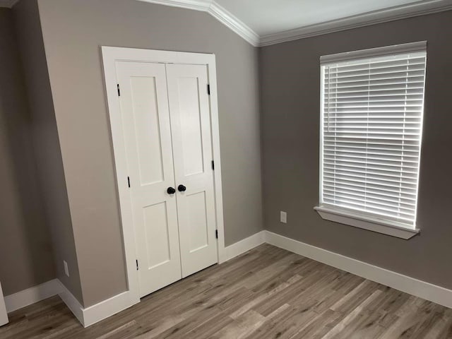 unfurnished bedroom with wood-type flooring, crown molding, and a closet