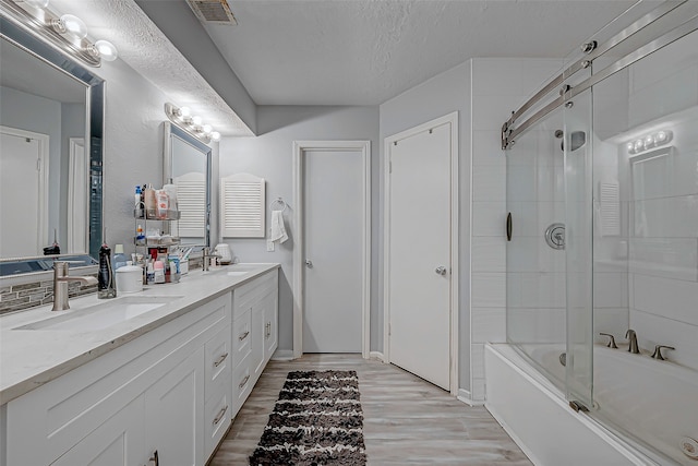 bathroom with hardwood / wood-style floors, vanity, a textured ceiling, and bath / shower combo with glass door