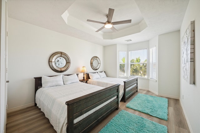 bedroom with ceiling fan, dark hardwood / wood-style flooring, and a tray ceiling