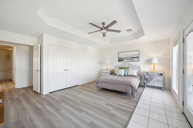 bedroom featuring light wood-type flooring, a closet, a raised ceiling, and ceiling fan