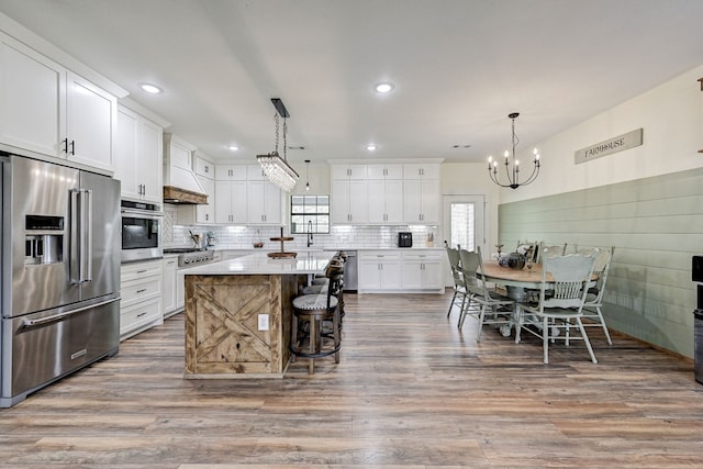 kitchen with hanging light fixtures, stainless steel appliances, a kitchen island, white cabinets, and hardwood / wood-style flooring