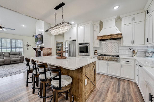 kitchen with pendant lighting, custom exhaust hood, white cabinets, light wood-type flooring, and appliances with stainless steel finishes