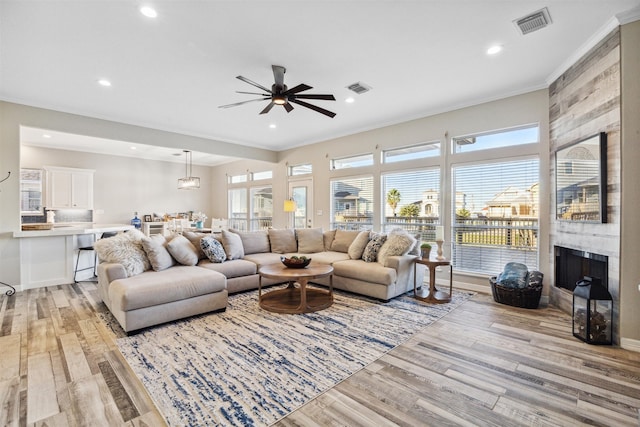 living room featuring a tile fireplace, light hardwood / wood-style floors, ceiling fan, and ornamental molding