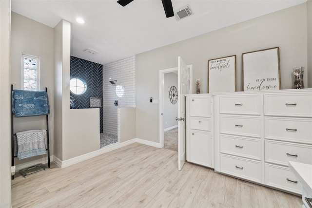 bathroom with ceiling fan, a tile shower, and wood-type flooring