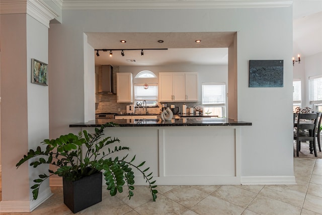 kitchen with wall chimney exhaust hood, plenty of natural light, kitchen peninsula, and dark stone counters