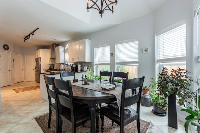 dining room with light tile patterned floors, rail lighting, plenty of natural light, and a notable chandelier