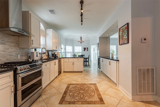 kitchen with sink, wall chimney exhaust hood, a healthy amount of sunlight, kitchen peninsula, and range with two ovens