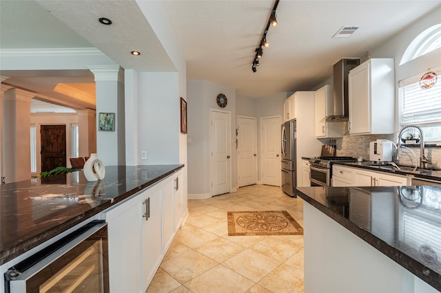 kitchen featuring ornate columns, white cabinetry, wall chimney exhaust hood, beverage cooler, and appliances with stainless steel finishes