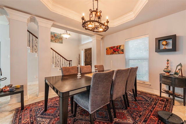 dining area with a chandelier, a raised ceiling, crown molding, and decorative columns