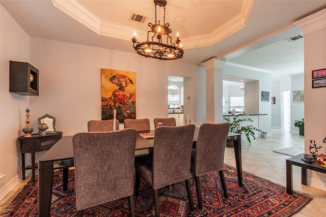 dining room featuring ornate columns, an inviting chandelier, crown molding, a tray ceiling, and light tile patterned floors