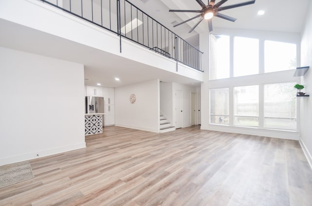 unfurnished living room with ceiling fan, light wood-type flooring, a towering ceiling, and a wealth of natural light