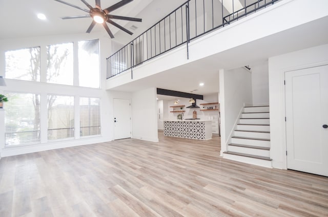 unfurnished living room featuring a healthy amount of sunlight, light wood-type flooring, and a towering ceiling