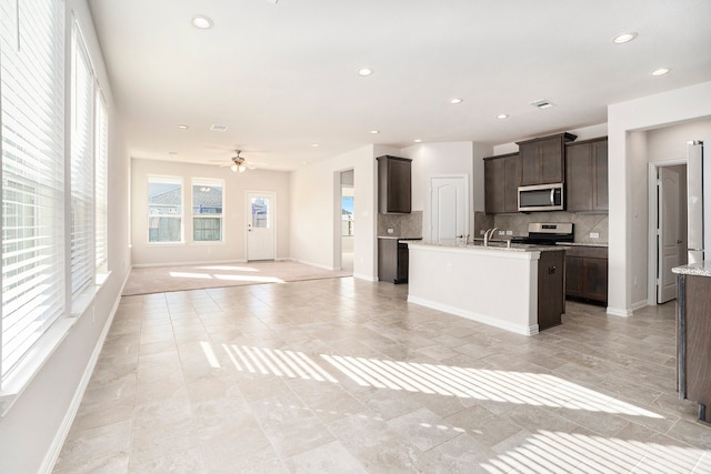 kitchen featuring appliances with stainless steel finishes, tasteful backsplash, dark brown cabinets, ceiling fan, and a kitchen island with sink