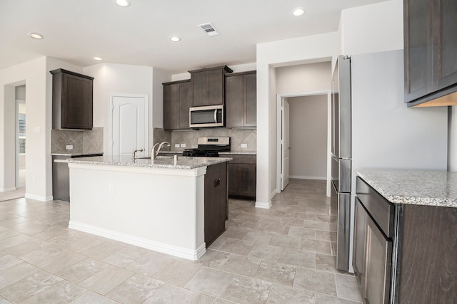 kitchen featuring appliances with stainless steel finishes, dark brown cabinetry, tasteful backsplash, and light stone counters