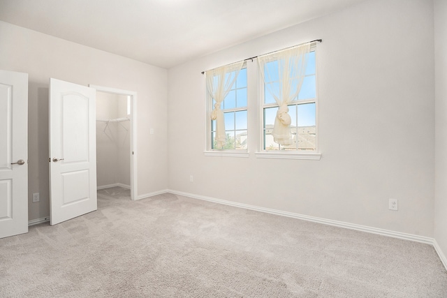 unfurnished bedroom with a walk in closet, a closet, and light colored carpet