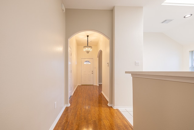 hallway with hardwood / wood-style floors, lofted ceiling, and a chandelier