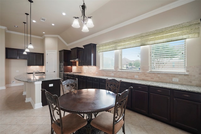 kitchen featuring decorative light fixtures, a healthy amount of sunlight, light stone counters, and a kitchen island with sink