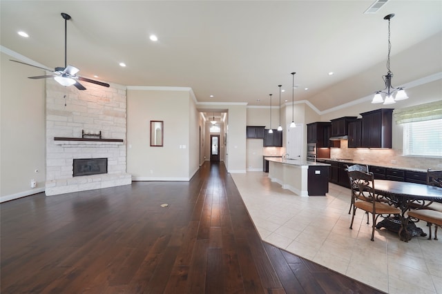 kitchen featuring a center island with sink, open floor plan, decorative light fixtures, light countertops, and backsplash