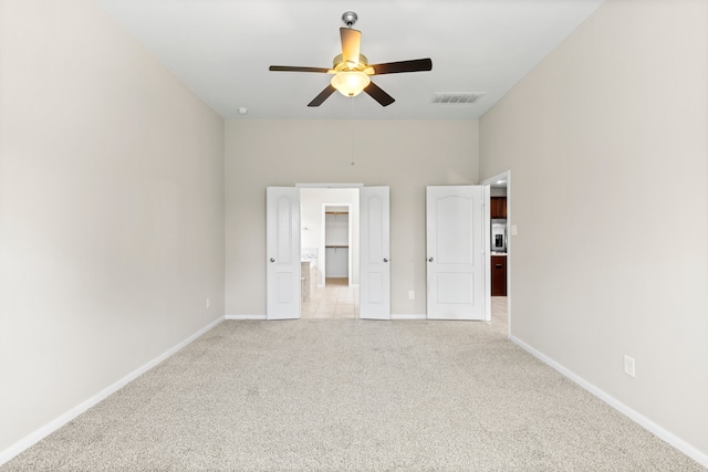 unfurnished bedroom with a walk in closet, light colored carpet, and ceiling fan