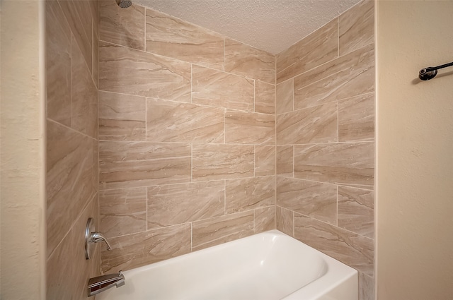 bathroom with a textured ceiling and tiled shower / bath