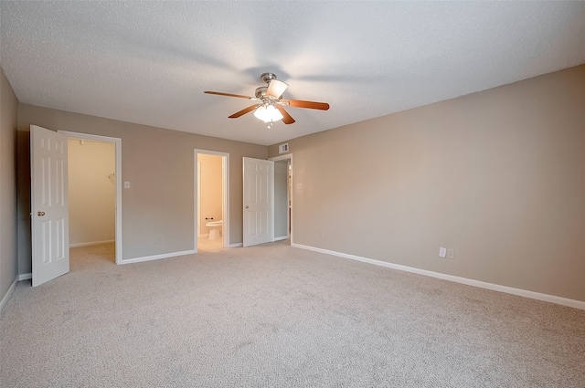 unfurnished bedroom featuring a textured ceiling, light colored carpet, ceiling fan, a spacious closet, and a closet