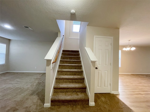 staircase with a textured ceiling, an inviting chandelier, and carpet flooring