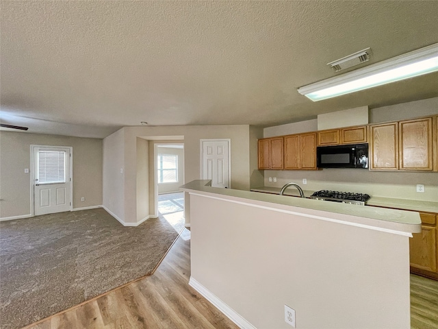 kitchen featuring a textured ceiling, range, a center island with sink, light wood-type flooring, and sink