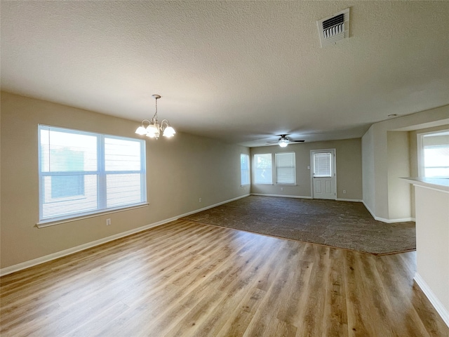 unfurnished living room with ceiling fan with notable chandelier, light wood-type flooring, and a textured ceiling